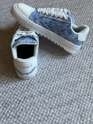 Numeris - Snygga sneakers från Numeris i blått och vitt med ett unikt mönster på sidan. Skorna har vita tjocka snören, vit tå och sula samt låg profil. Perfekta för dig som vill ha något stilrent men ändå sticker ut.