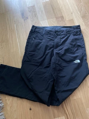 Svarta friluftsbyxor från The North Face- strl 6/S - Säljer ett par svarta friluftsbyxor från The North Face med klassisk logga på benet. Byxorna har raka ben, bälteshällor och dragkedjeficka på sidan. Perfekta för en tur i skogen eller vandring