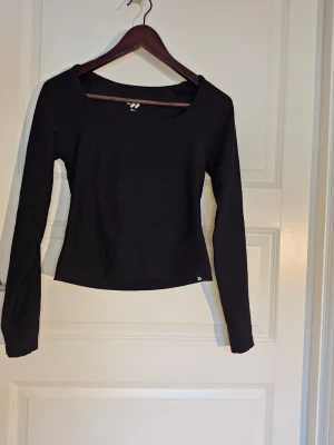 Svart långärmad topp med fyrkantig ringning - Snygg svart långärmad topp med en modern fyrkantig ringning. Toppen har en slim passform och är tillverkad i ett stretchigt material som sitter skönt på kroppen. Perfekt att styla med jeans eller kjol för en clean look.  Tröjan kommer från lager 157.   Knappt använd 