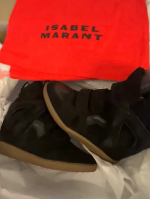 Isabel Marant svarta sneakers - Svarta sneakers från Isabel Marant med kilklack och kardborreband. Skorna har en chunky siluett, ovandel i mocka och detaljer i läder. Yttersulan är i gummi med brun ton. Perfekta för dig som vill ha både stil och höjd.
