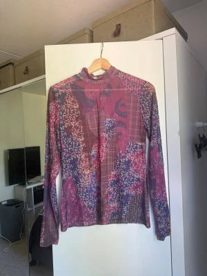 Mönstrad långärmad polotopp - Säljer en långärmad polotopp med patchworkmönster i lila, rosa och blå toner. Toppen har en smal passform och är tillverkad i ett tunt, stretchigt syntetmaterial. Perfekt för dig som gillar unika och färgglada plagg! Från märket Odd Molly i storlek 3 som enligt deras storlekguide motsvarar en storlek L. Mycket fint skick, jag hittar inga synliga anmärkningar eller defekter. 