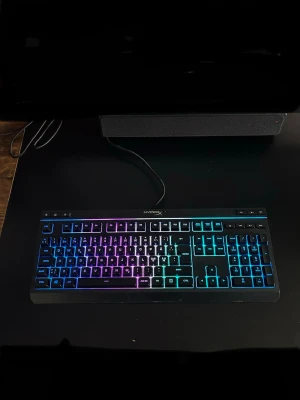 HyperX RGB tangentbord med sladd - Säljer ett HyperX tangentbord med RGB-belysning som lyser i flera färger. Tangentbordet har en klassisk rektangulär form och ansluts med USB-kabel. Perfekt för gaming eller arbete där du vill ha snygg belysning på skrivbordet.