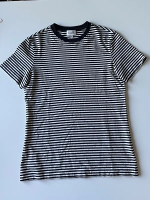 Randig t-shirt från & Other Stories - Säljer en svartvit randig t-shirt från & Other Stories i storlek XS. T-shirten har korta ärmar, rund halsringning med svart kant och är gjord i mjuk bomull.