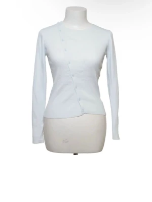 Zara topp - Säljer en ljusblå långärmad topp med sned knäppning framtill. Toppen har en slim passform och är tillverkad i ett mjukt material som sitter snyggt på kroppen. Perfekt att styla med jeans eller kjol för en clean look.