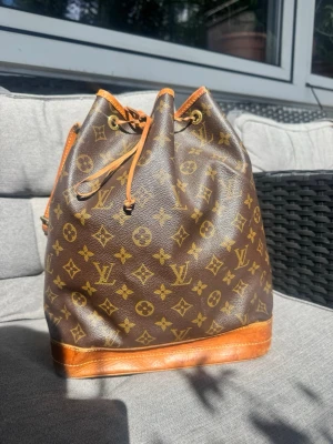 Louis Vuitton Monogram Noé bucket bag - Säljer en klassisk brun Louis Vuitton Noé bucket bag i monogram canvas med detaljer i läder. Väskan har dragskostängning och justerbar axelrem. Perfekt för dig som gillar tidlös design och vill ha plats för allt du behöver.     