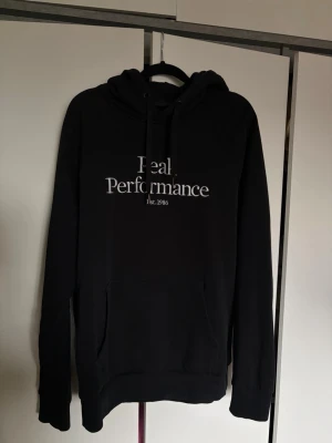 Svart hoodie Peak Performance - Snygg svart hoodie från Peak Performance med broderad vit logga och texten 