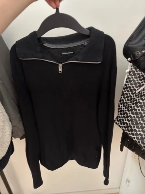Svart stickad tröja med dragkedja - Säljer en svart stickad tröja från Jack & Jones med halv dragkedja och krage. Tröjan har lång ärm och enkel, stilren design som passar till det mesta. Perfekt för dig som gillar en clean och klassisk look.
