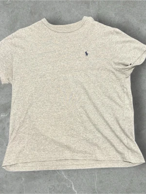 Gråmelerad t-shirt från Polo Ralph Lauren - Snygg gråmelerad t-shirt från Polo Ralph Lauren med klassisk blå logga broderad på bröstet. T-shirten har rund halsringning och korta ärmar. Perfekt basplagg i mjuk bomull som passar till allt.