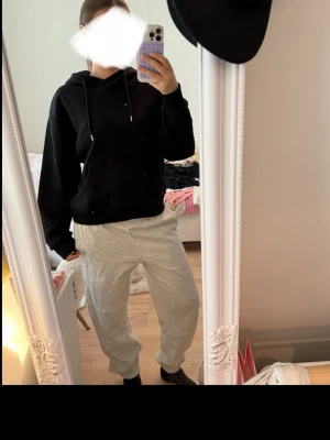 Svart hoodie med huva och snören - En klassisk svart hoodie med huva och justerbara snören. Hoodien har en avslappnad passform och ribbade muddar vid ärmar och midja. Perfekt för en chill och bekväm stil. Materialet ser ut att vara mjukt och skönt, troligen bomullsblandning.