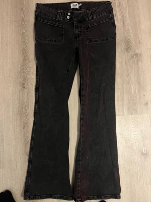 Svarta bootcut jeans med låg midja - Ett par svarta jeans med bootcut-modell och låg midja. Jeansen har dubbla knappar framtill, två framfickor och två bakfickor. Snyggt slitna detaljer och klassisk femficksdesign. Perfekta för en trendig och avslappnad stil.