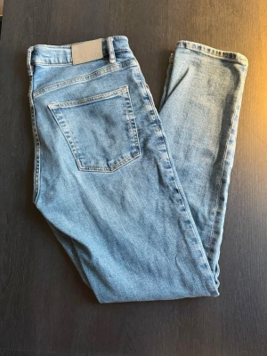 Ljusblå raka jeans - Säljer ett par ljusblå jeans med rak passform och klassisk femficksdesign. Jeansen har normal midja och är tillverkade i denim med en snygg tvätt. Perfekta för en avslappnad och trendig look.
