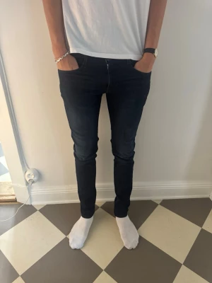 Mörkblå slim fit jeans herr Replay Anbass  - Säljer ett par mörkblå slim fit jeans med klassisk femficksdesign och smal passform. Jeansen har normal midja och är tillverkade i ett stretchigt material som sitter snyggt längs benen. Perfekta för en clean och stilren look. Storlek 31