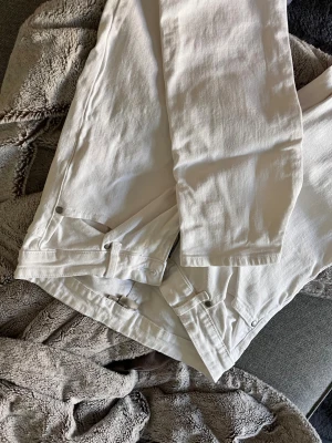 Vita raka jeans med hög midja - Säljer ett par vita jeans med rak passform och hög midja. Jeansen har klassiska fem fickor, dragkedja och knapp framtill. Materialet är kraftigt denim i bomull. Perfekta för en clean och stilren look. 