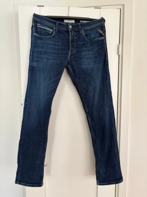 Mörkblå raka jeans från Replay - Snygga mörkblå jeans från Replay med raka ben och klassisk femficksmodell. Jeansen har kontrastsömmar och en liten logga på bakfickan. Tillverkade i slitstark denim med en tidlös look som passar till det mesta. Modellen på jeansen är Grover. 