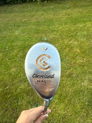 Cleveland Halo 22° hybridklubba - Säljer en Cleveland Halo hybridklubba med 22 graders loft. Klubban har en silverfärgad metallhuvud med tydliga linjer på träffytan och svart detalj vid skaftet. Perfekt för dig som vill ha extra kontroll och längd på golfbanan.