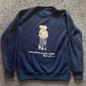  Polo Ralph Lauren sweatshirt - Mörkblå sweatshirt från Polo Ralph Lauren med ikoniska Polo Bear-trycket på bröstet. Rund halsringning, ribbade muddar vid ärmslut och nederkant. Perfekt för en avslappnad och stilren look. Priset kan diskuteras 