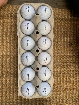  A- klass Srixon golfbollar  - Tolv vita golfbollar från Srixon, förvarade i en äggkartong. Bollarna har siffror i olika färger och klassisk dimple-yta för bra flyg. Perfekt för dig som vill fylla på golfväskan inför nästa runda.