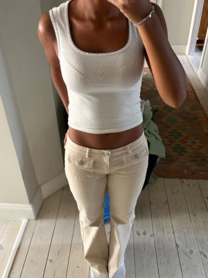 Vit prickig topp - Söt vit topp med små blå prickar. Toppen är ärmlös med bredare axelband och har en fyrkantig ringning med diskret spetskant. Perfekt till alla outfits.