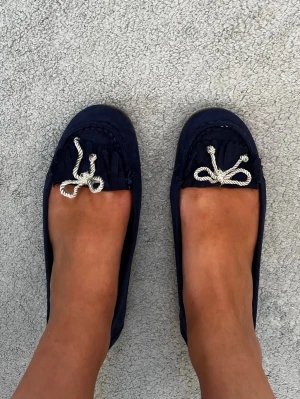 Marinblå seglarskor med repdetalj - Säljer ett par marinblå seglarskor från mywear med vita repdetaljer i form av rosetter framtill. Skorna har en klassisk låg profil och randigt innerfoder. Perfekta för en avslappnad och stilren look till sommaren.