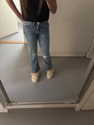 Blå slitna jeans från Gina Tricot - Säljer ett par blå jeans från Gina Tricot i storlek 146. Jeansen har utsvängda ben, slitningar på knäna och klassisk femficksmodell. Perfekta för en avslappnad och trendig look.