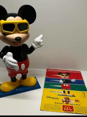 Musse Pigg Happy Meal 1999 - Unik samlarleksak från McDonald’s Happy Meal 1999! Musse Pigg med 4 roliga funktioner: •Huvud: 3D-bildvisare med roterande hjul, visar Disneyland Paris-bilder •Överkropp: vattenpistol •Byxor: kikare •Fötter: rullar med stämplar på (utan bläck)  Perfekt för Disney-samlare eller nostalgientusiaster. Komplett och i gott skick. Kan även skicka med ett reklablad för det som fanns i en kalle anka tidning.  #Mickey Mouse