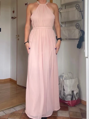 Balklänning haulterneck - Elegant långklänning i ljusrosa med halterneck och glittriga detaljer längs halsringningen. Klänningen har plisserad kjol, slits vid benet och öppen rygg. Bra som examen, bal eller finklänning. Går inte att köpa längre