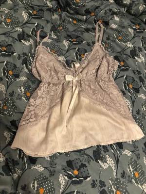 En jätte fin vit topp som kan vara perfekt alla tillfällen  - Söt blus i vit med tunna axelband och spetsdetaljer upptill. Framtill sitter en dekorativ rosett i satin. Materialet är glansigt och mjukt, troligen polyester eller liknande. Spetsen har blommönster och blusen har en lös, luftig passform.