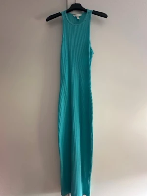 Turkos ribbad långklänning - En turkos ribbad långklänning som är ärmlös. Klänningen har en öppen rygg och är gjord i ett stretchigt material. Använd 1 gång. 