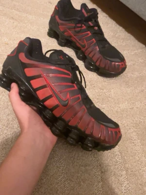 Nike Shox svarta och röda sneakers - Nike Shox sneakers i svart och rött med ikoniska fjädrande sulor. Skorna har en sportig design med röda detaljer och swoosh-logga på sidan. Ovandelen är i textil och syntet, och sulan har den klassiska Shox-dämpningen för extra komfort. Det är inget fel på dom och Dome väldigt bekväma och ha på sig men det bara några märken på sulan som man inte ser på långt håll