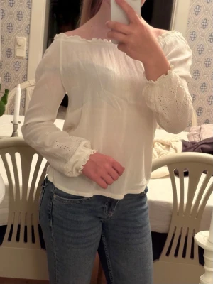 Vit  blus med spetsdetaljer - Säljer en söt vit offshoulder blus med långa ärmar och fina spetsdetaljer vid ärmsluten. Blusen har en lätt rynkad kant upptill och är gjord i ett tunt, luftigt material som känns perfekt för vår och sommar. Passar till både jeans och kjol!