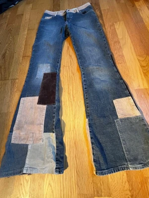 Patchwork jeans med vida ben - Skitcoola blåa flared jeans med flera stora patchwork-lappar i olika färger och material, bland annat manchester. Lite slitage längst ned som visas på bild 5, annars i mycket bra skick. Köpta second hand, strl W28 på lappen och skulle gissa på L34. Ingen stretch💗