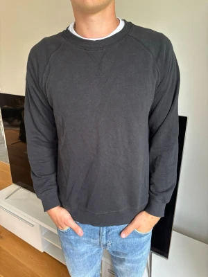 Svart sweatshirt från 157 - En enkel och stilren svart sweatshirt från 157 med rund halsringning och ribbade muddar vid ärmslut och nederkant. Tillverkad i mjukt material som känns skönt mot huden. Perfekt att matcha med jeans eller joggers.
