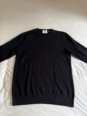 Bläck Tröja - Klassisk svart tröja från Bläck i 100% Pima bomull. Tröjan har rund halsringning, långa ärmar och ribbade muddar vid ärmslut och nederkant. Perfekt basplagg som funkar till det mesta och är enkel att matcha med andra plagg.