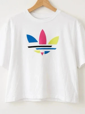 Vit t-shirt med färgglad Adidas-logga - Vit t-shirt med en stor Adidas-logga i blått, rosa och gult framtill. T-shirten har korta ärmar och en avslappnad passform. Perfekt för dig som gillar sportig och trendig stil.