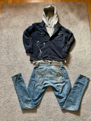 Ljusblå Nudie Jeans  - Säljer ett par ljusblå jeans från Nudie Jeans med klassiska bakfickor och kontrastsömmar. Jeansen har en rak passform och är tillverkade i denim med feta slitningar. Perfekta för en chill och laidback look. Storlek = W28, L34. Hör av er vid frågor! 