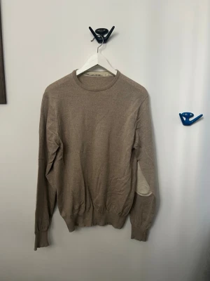 Beige stickad tröja med rund hals ( stenströms ) - En enkel och stilren beige stickad tröja med rund halsringning och långa ärmar. Tröjan har ribbade muddar vid ärmslut och nederkant. Perfekt för lager på lager och passar till det mesta i garderoben.