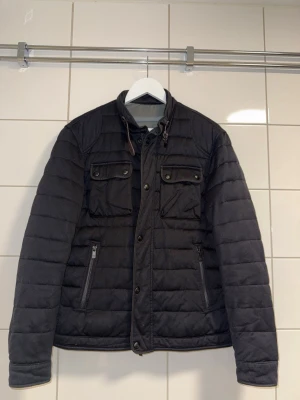 Massimo Dutti Dunjacka / Quiltad Jacka Svart Herr Strl L - Snygg och stilren Massimo Dutti jacka i svart, storlek L. Quiltad/puffad modell med hög krage, flera praktiska fickor och snygga detaljer. Väldigt lättmatchad och passar perfekt till både vardag och en mer uppklädd stil.  • Märke: Massimo Dutti • Storlek: L / 185–104A • Färg: Svart • Modell: 3406 • Skick: Fint begagnat skick  ⚠️ En liten söm på baksidan har släppt, men det är diskret och inget man direkt tänker på när jackan används. Se bild för tydlighet.  📦 Skickas snabbt och välpaketerat.