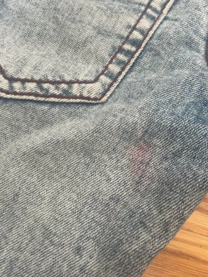 Blå bootcut jeans med kontrastsömmar - Säljer ett par ljusblå bootcut jeans med tydliga kontrastsömmar och klassiska bakfickor. Jeansen har en lätt tvättad look och vida ben. Materialet är denim i bomull. Perfekta för dig som gillar retrostil och vill ha ett par jeans som sticker ut. Varan har en liten rosa fläck nära vänster bakficka.