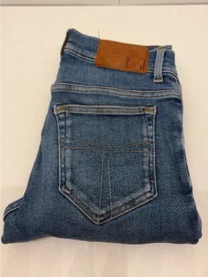 Tiger of Sweden jeans  - Säljer ett par klassiska blå jeans i rak modell med fem fickor och kontrastsömmar. Jeansen har en brun läderpatch i midjan och är tillverkade i denim med snygg tvätt. Perfekta till en avslappnad stil och passar till det mesta.