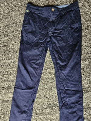Lacoste chinos - Snygga mörkblå chinos från Lacoste i storlek 14 (164 cm). Klassisk modell med rak passform och broderad Lacoste-logga framtill. Byxorna är i fint begagnat skick utan hål eller fläckar. Nvtvättade och reda att användas. Behöver bara strykas för att bli helt släta. Kommer från ett djur- och rökfritt hem. Skickas snabbt