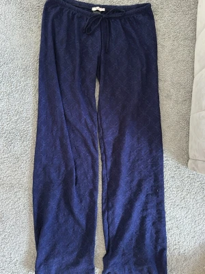 Lågmidjade mjukisbyxor - Ett par mörkblå loungewear-byxor med avslappnad passform och dragsko i midjan. Byxorna har ett diskret mönster i tyget och är tillverkade i ett mjukt, bekvämt material som passar perfekt för hemmamys eller chill dagar.