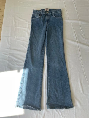 Blå utsvängda jeans med medelhög midja - Snygga blå jeans med medelhög midja och utsvängda ben. Klassisk femficksmodell i mjukt denimtyg. Perfekta för dig som vill ha ett Basic jeans par jeans.