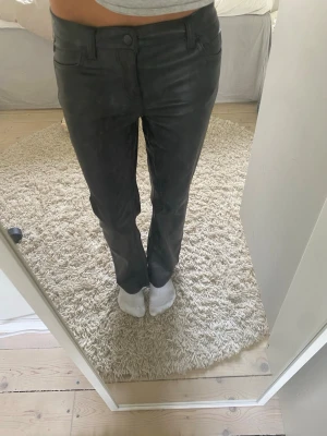 Svarta bootcut byxor i skinnimitation - Säljer ett par svarta byxor i skinnimitation med bootcut-modell och normal midja. Byxorna har klassiska fickor fram och bak. Snyggt glansigt material som ger en cool look.