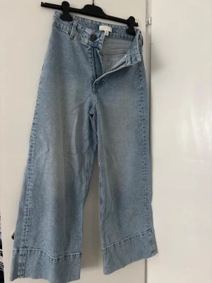 Ljusblåa vida jeans med hög midja - Säljer ett par ljusblå jeans med hög midja och riktigt vida ben. Jeansen har klassisk femficksmodell, bälteshällor och dragkedja med knapp. Perfekta för en avslappnad och trendig look. Materialet är denim i bomull.