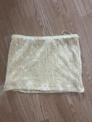 Gul paljettkjol från Gina Tricot - Kort gul kjol från Gina Tricot med paljettdetaljer som ger ett glittrigt intryck. Kjolen har en rak passform och är tillverkad i ett mjukt syntetmaterial. Perfekt för dig som vill sticka ut lite extra. Ny utan prislapp