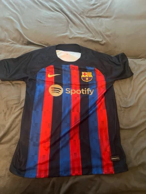 Barcelona matchtröja Nike röd/blå - Säljer en FC Barcelona matchtröja från Nike med klassiska röda och blå vertikala ränder. Tröjan har klubbmärke, Nike-logga och Spotify som sponsor framtill samt UNHCR-logga bak. Tillverkad i lätt och ventilerande material, perfekt för fotboll eller träning.