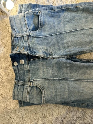 Ljusblå raka jeans med sömdetaljer - Säljer ett par ljusblå jeans med raka ben och markerade sömmar framtill. Jeansen har klassiska fem fickor, bälteshällor och dragkedjegylf. Materialet är denim i bomull och de har en avslappnad passform som passar till många olika stilar.