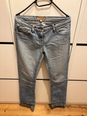Ljusblå raka jeans från Etam - Säljer ett par ljusblå jeans från Etam med klassisk femficksmodell och raka ben. Jeansen har normal midja, snygga slitningar och kontrastsömmar. Perfekta för en avslappnad och trendig look.