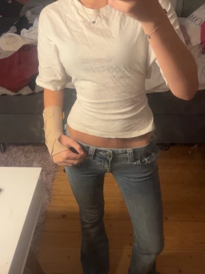 Vit croppad topp med knyt i ryggen - Säljer en vit croppad topp med korta ärmar. Toppen har en snygg detalj med knytband i ryggen som ger en unik look. Tillverkad i ett tunt, lätt material som sitter tajt och framhäver midjan. Perfekt för dig som gillar trendiga och stilrena plagg.
