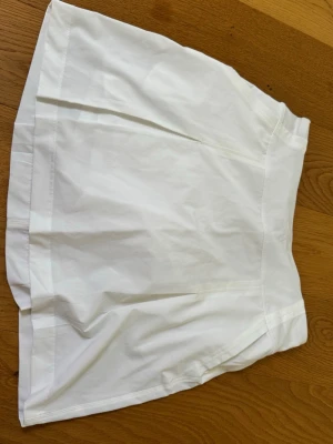 Vit skort med sportig känsla - Snygg vit golf skort med bred linning och diskreta sömdetaljer. Kjolen har inbyggda shorts i meshmaterial för extra komfort och rörelsefrihet. Perfekt för en aktiv och trendig look. Materialet känns lätt och luftigt.